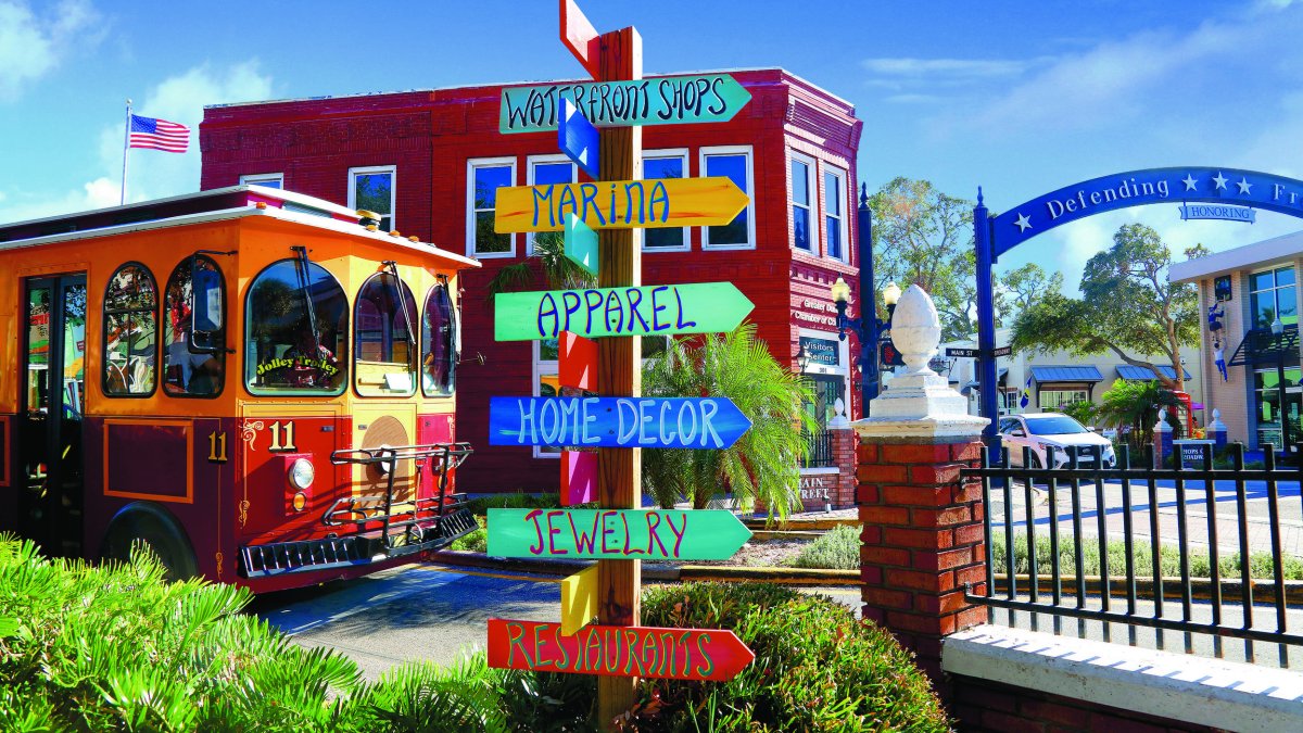 A colorful direction sign is in front of a trolley and shops.