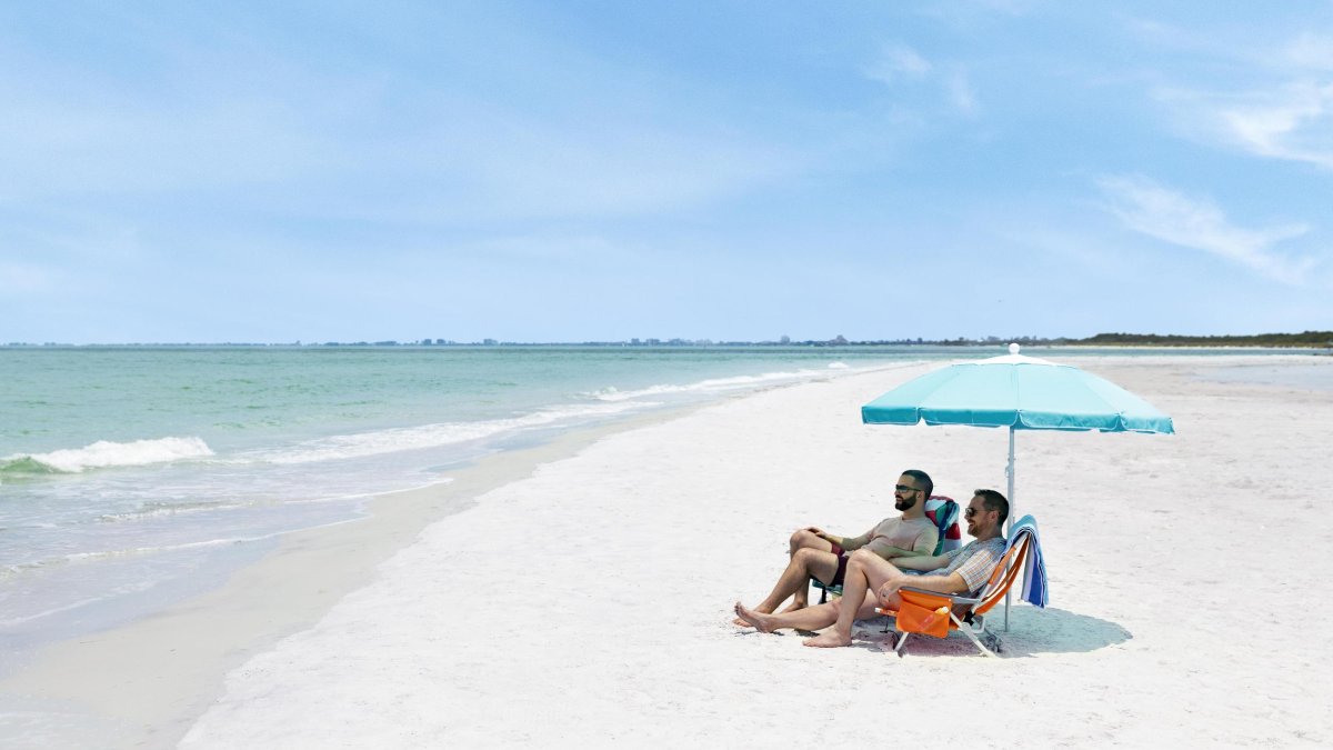 Couple sits under an umbrella on a wide, white-sand beach