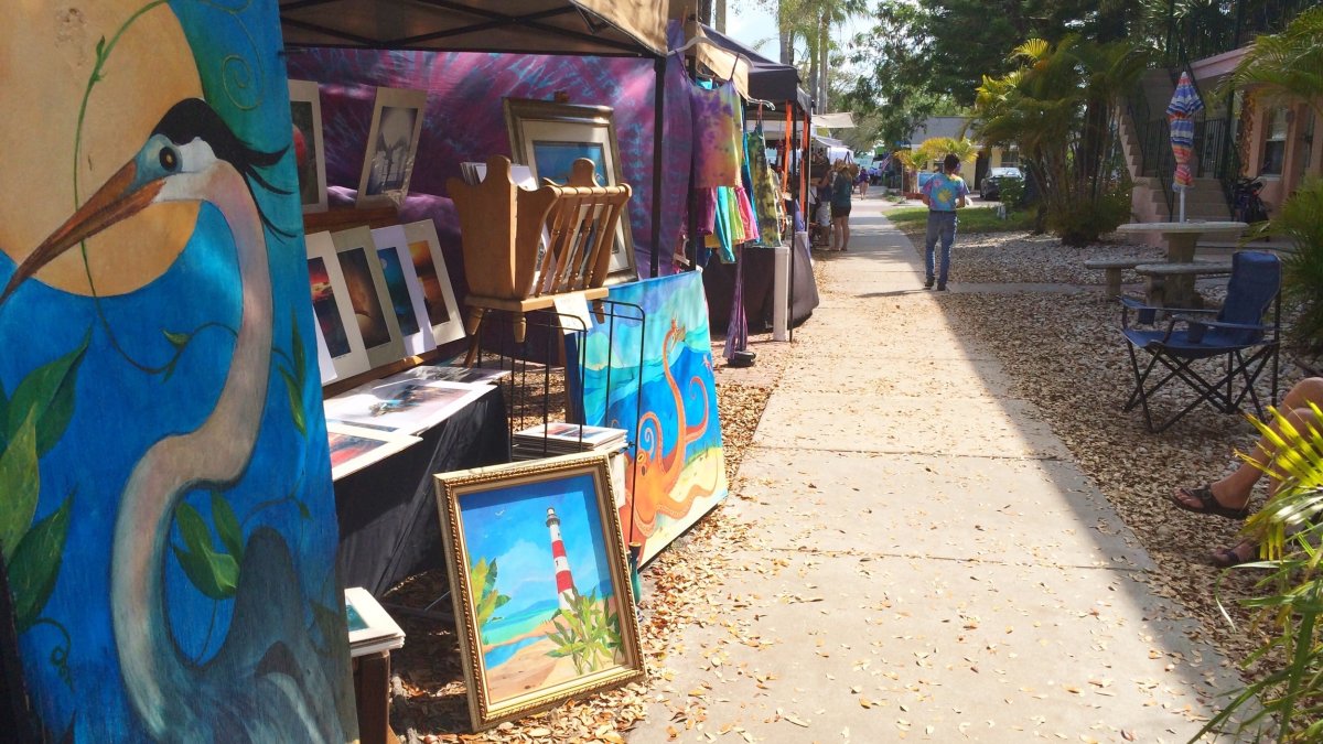 Tents filled with paintings and other artwork for sale line a sidewalk.