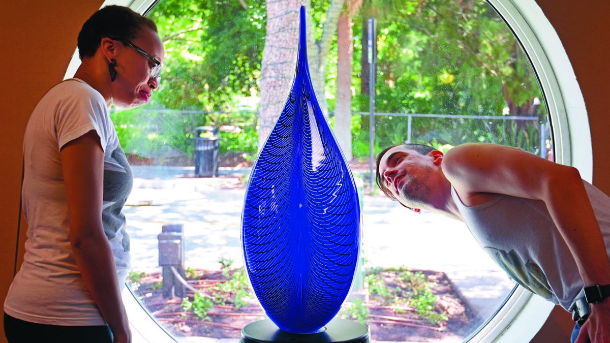 A woman and man look at a tall blue glass sculpture.