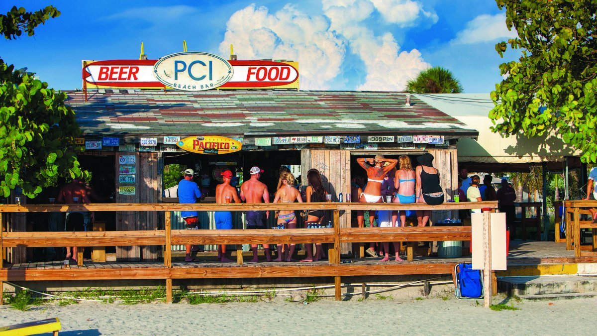 People in swimsuits drink on wooden deck at beach bar