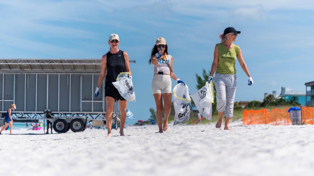 three women with trash bags at a beach clean up