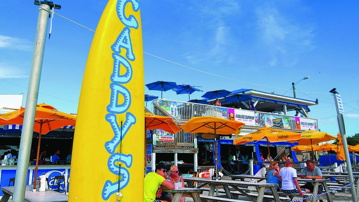 A yellow surfboard with "Caddy's" at a casual restaurant with picnic tables on the beach