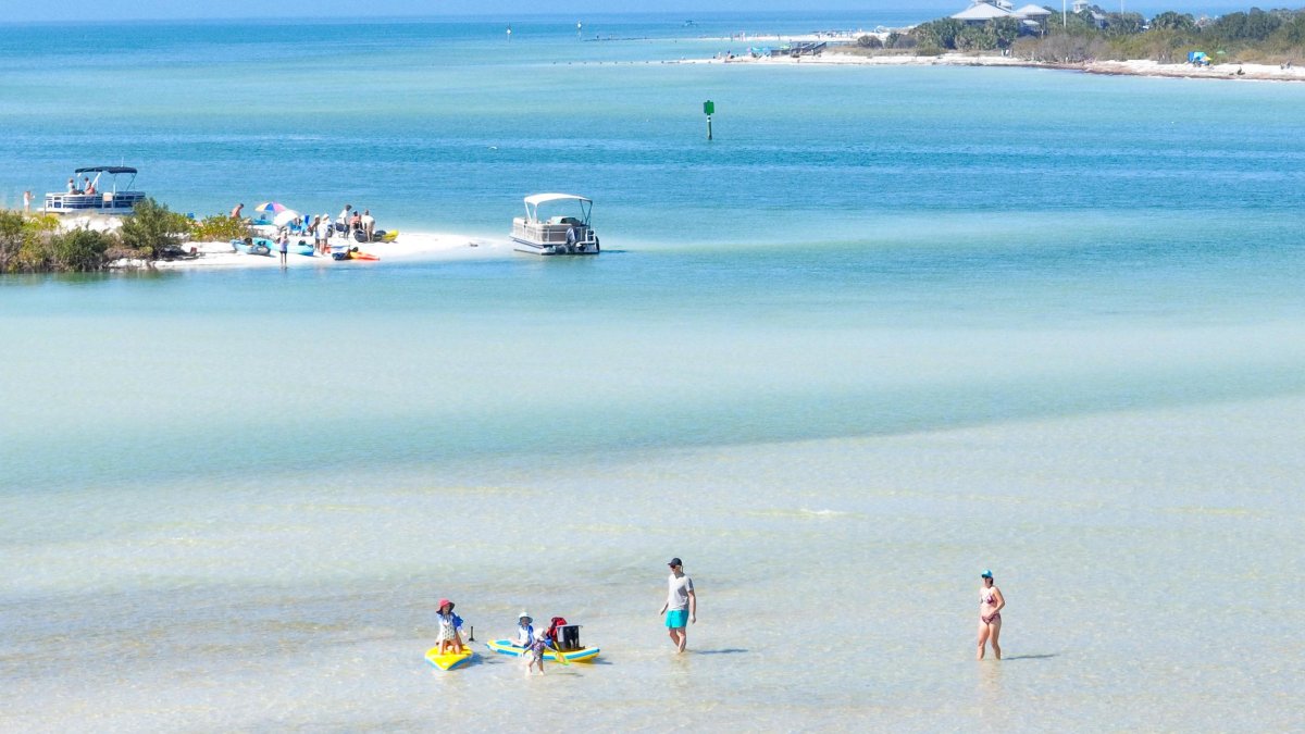 People wade in clear water with two islands nearby.