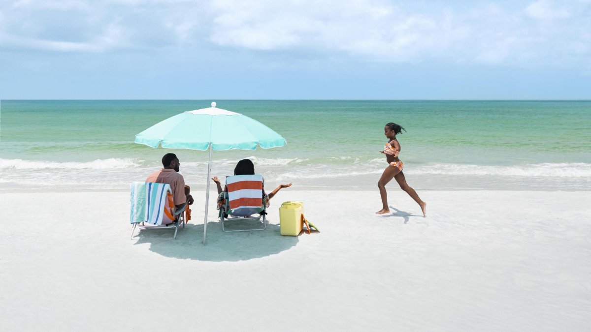 Girl running on the beach toward parents under an umbrella