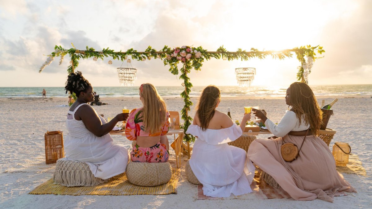 Four women enjoy an elaborate picnic on the beach