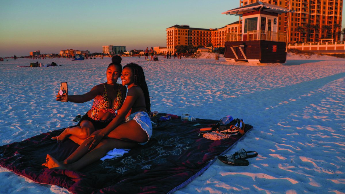 Two women sitting on the beach at sunset take a selfie