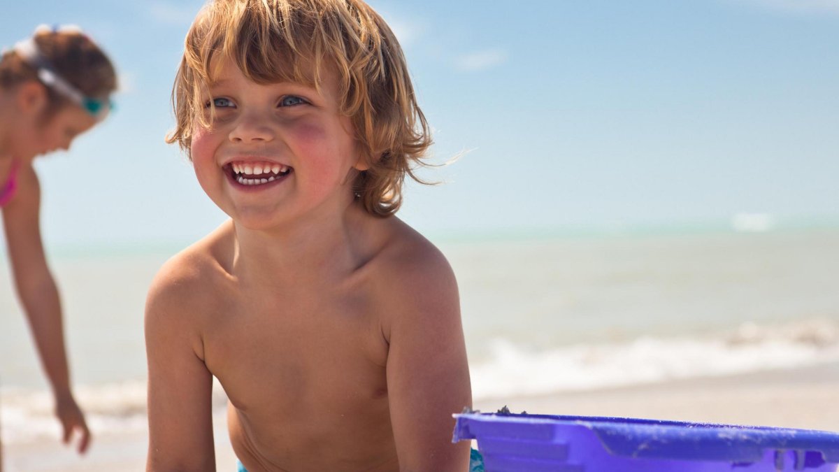 Smiling boy with a purple pail on the beach.