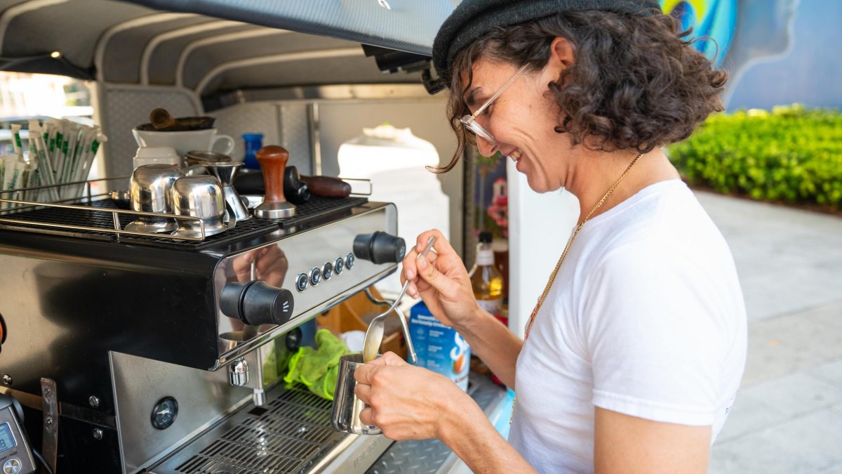 a person with curly hair and a cap steaming milk at Cafe Tuk Tuk