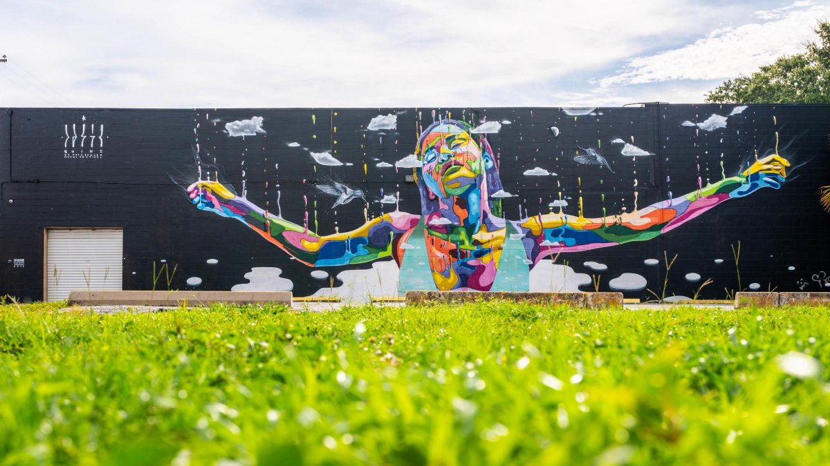 a vibrantly colored mural of a young woman with arms outstretched painted on a black building