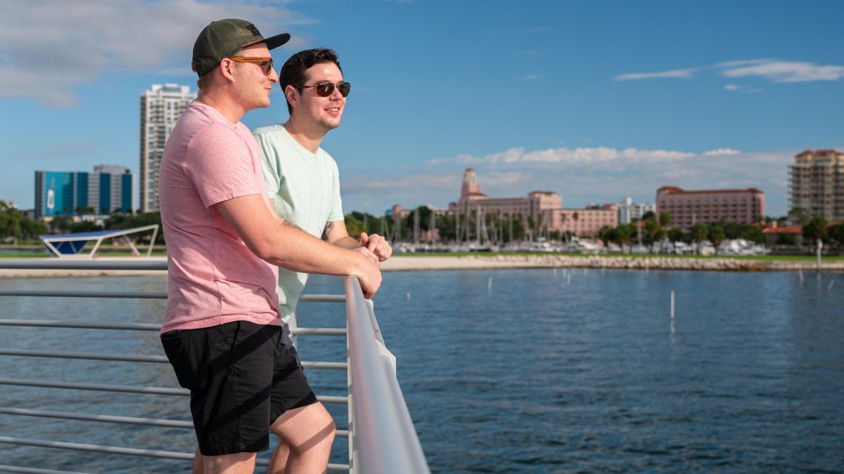 two men stand near a railing looking out over the water near the St. Pete Pier