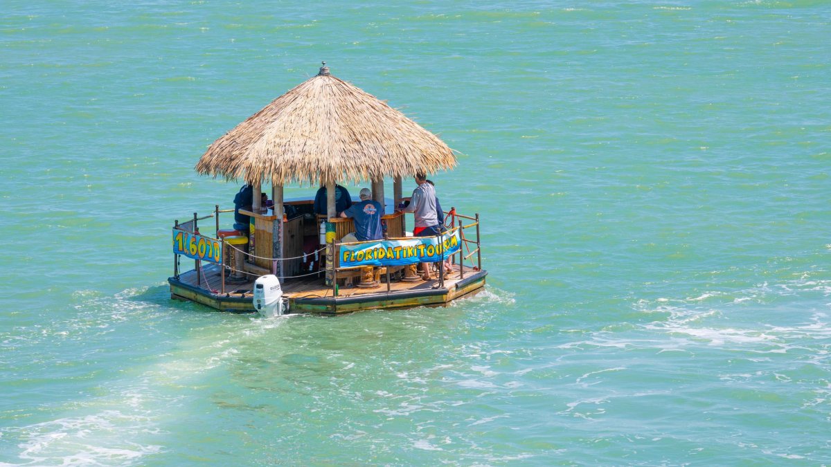 A group of friends relax in a thatched tiki hut boat as it floats along the water.