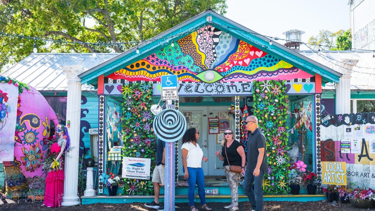 three people stand outside a brilliantly colored and whimsical building