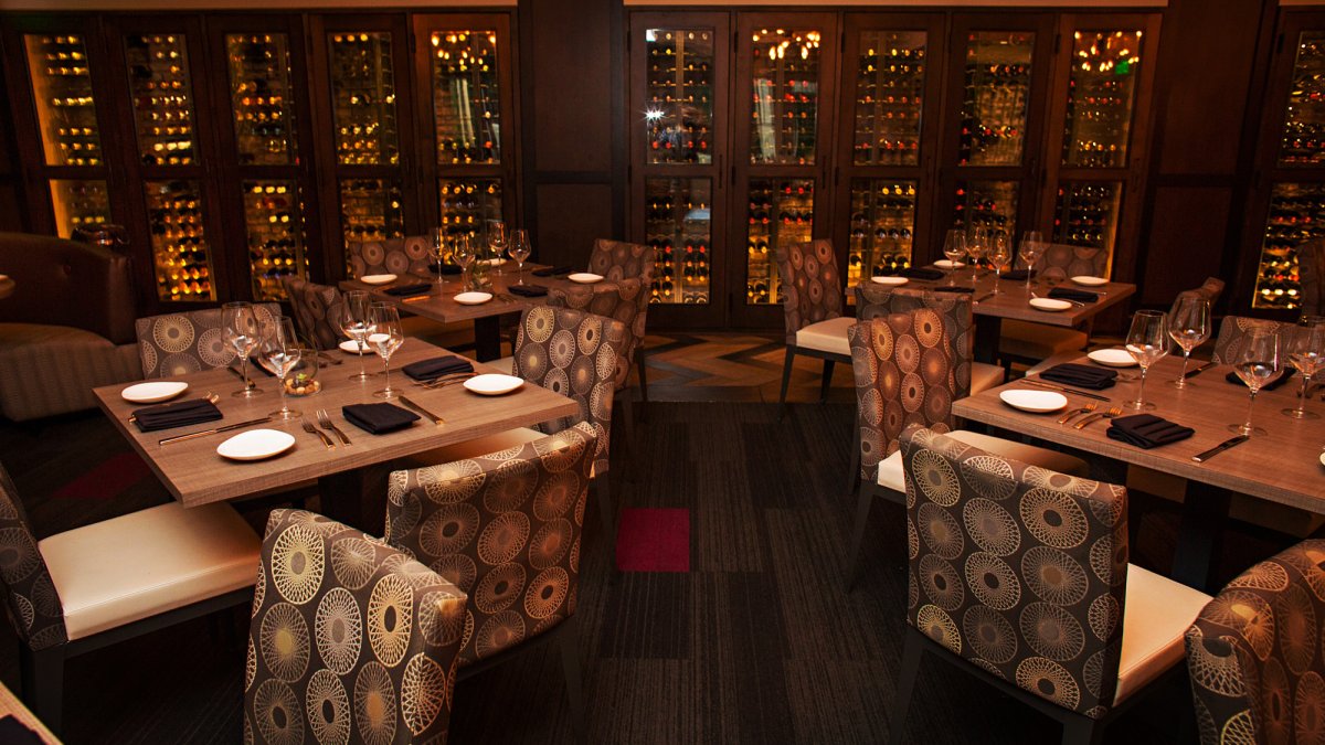 A dim moody dining room with a wine wall in the backdrop