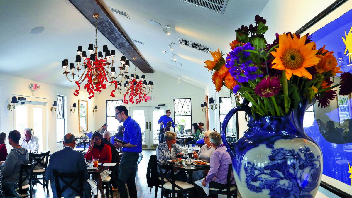 Diners enjoy their meals inside a cafe surrounded by flower decorations.