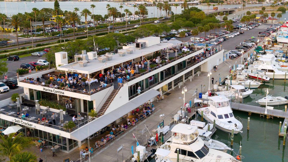 An exterior aerial view of a two-story restaurant with boats in a marina in front