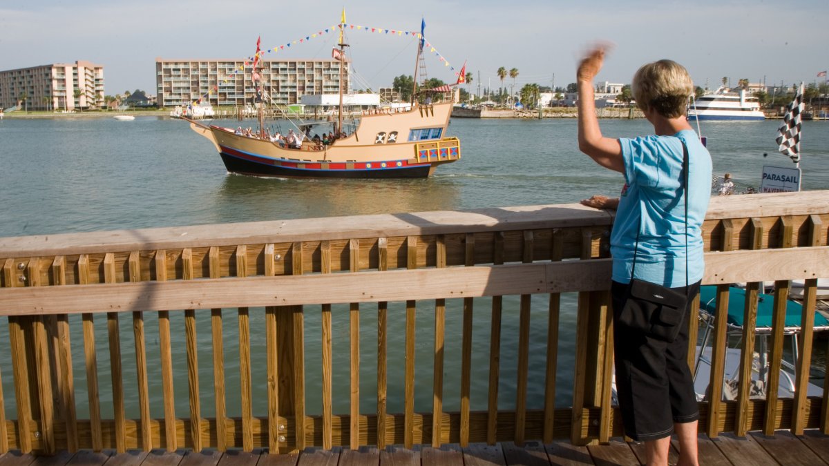 A woman on a dock waves at a passing pirate ship boat tour.
