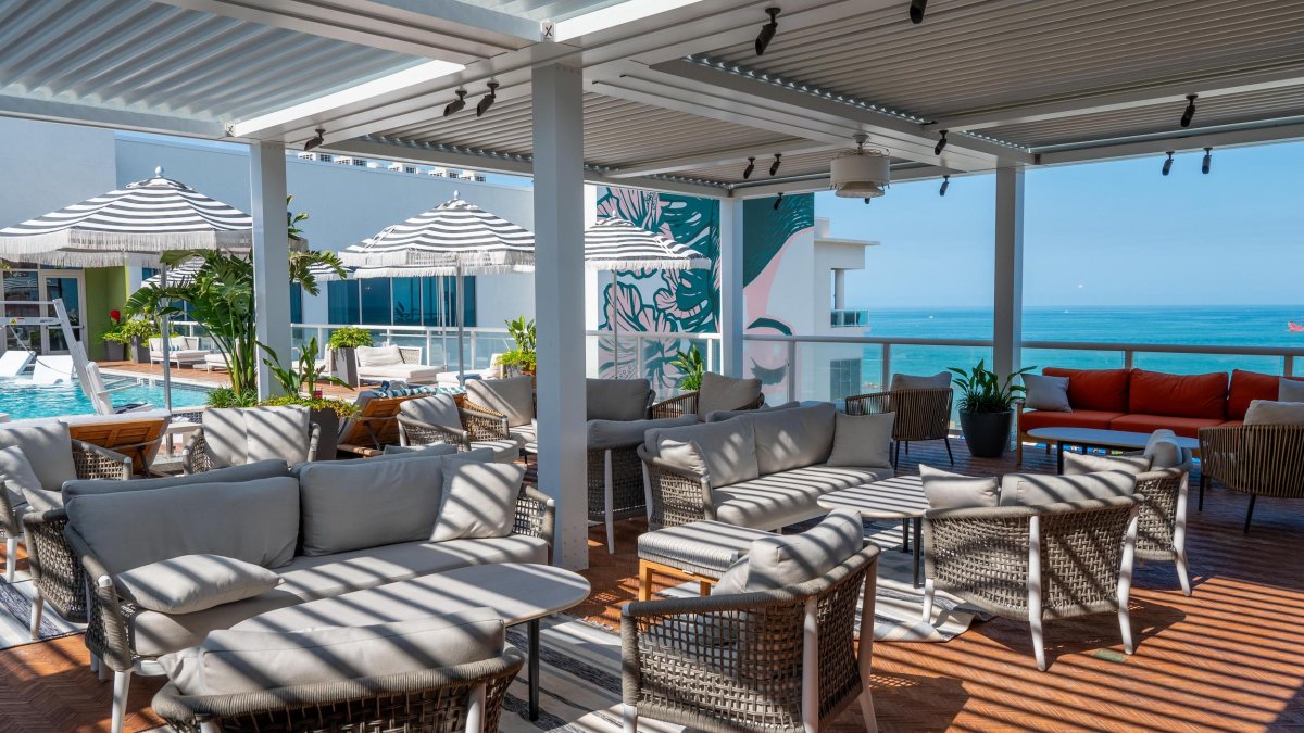 a beautiful rooftop bar with tables and chairs next to a swimming pool with umbrellas for shade with a view of the turquoise gulf of mexico