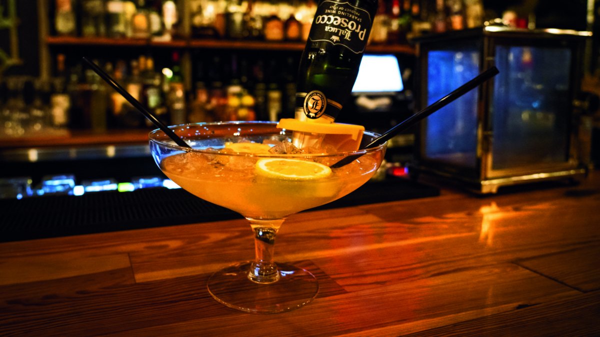 A photo of a pink cocktail with two straws on a bar