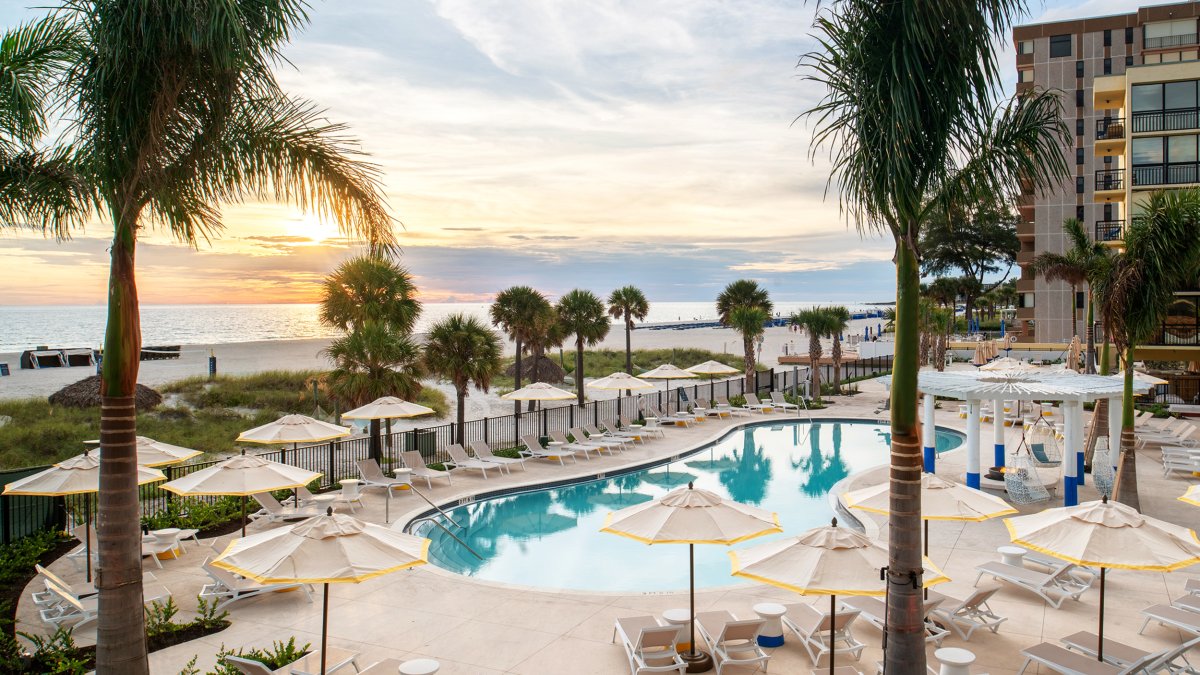palm trees in foreground and a pool with chairs and umbrellas around it near the beach at sunset at Sirata Resort