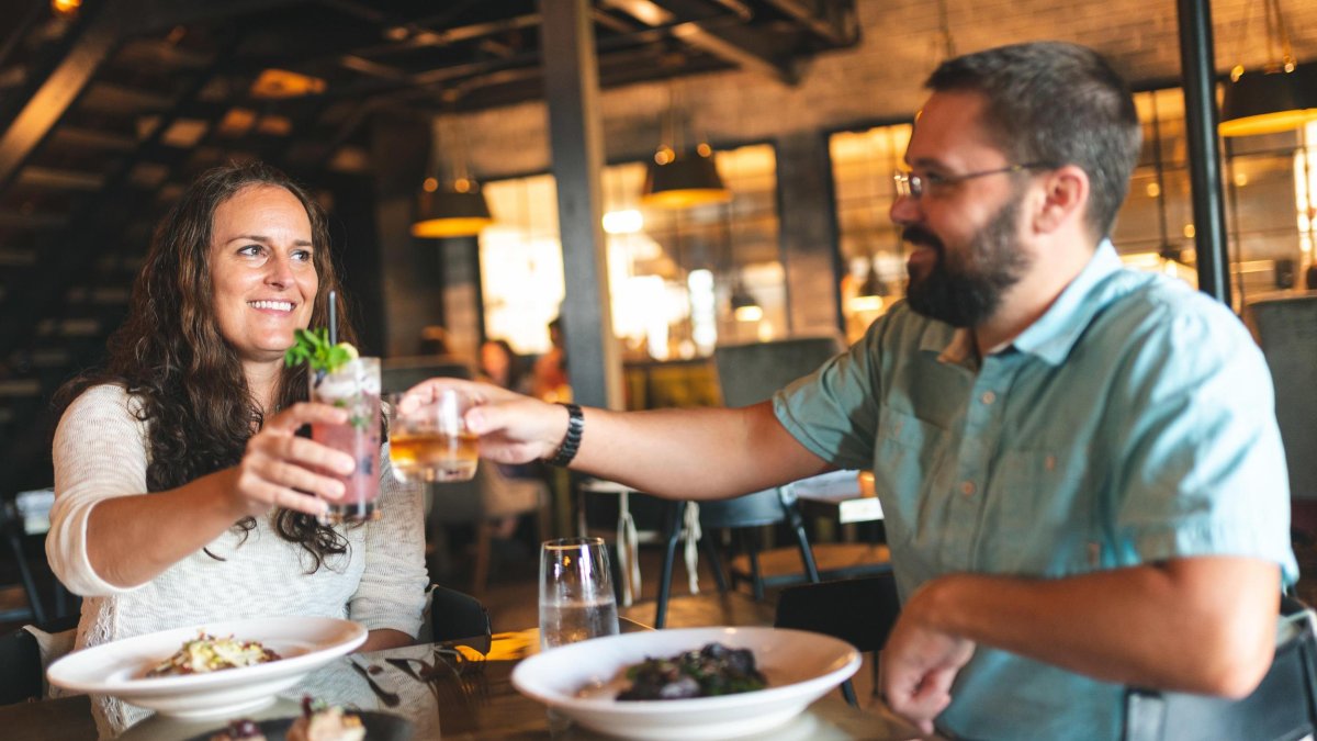 Two diners cheers with cocktails at a restaurant table