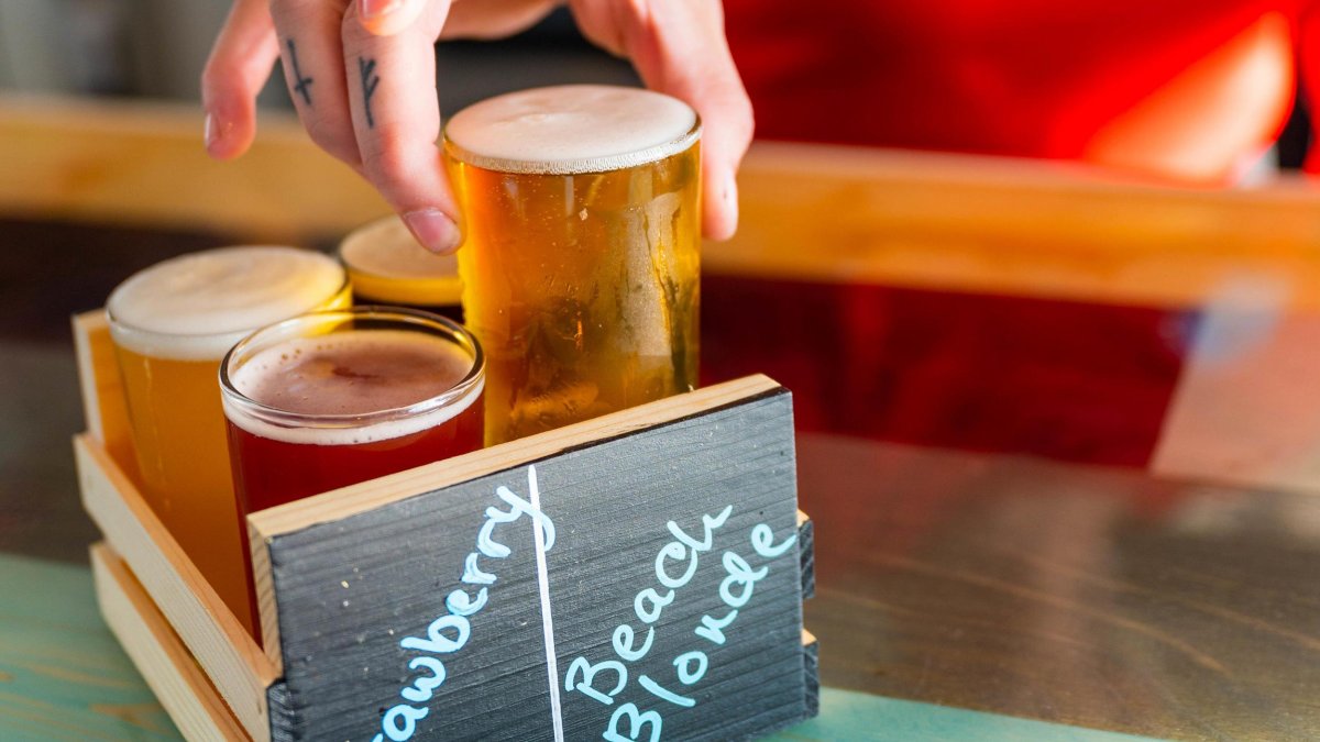 a flight of 4 different flavored beers in a carrying box with a person's hand placing a beer inside