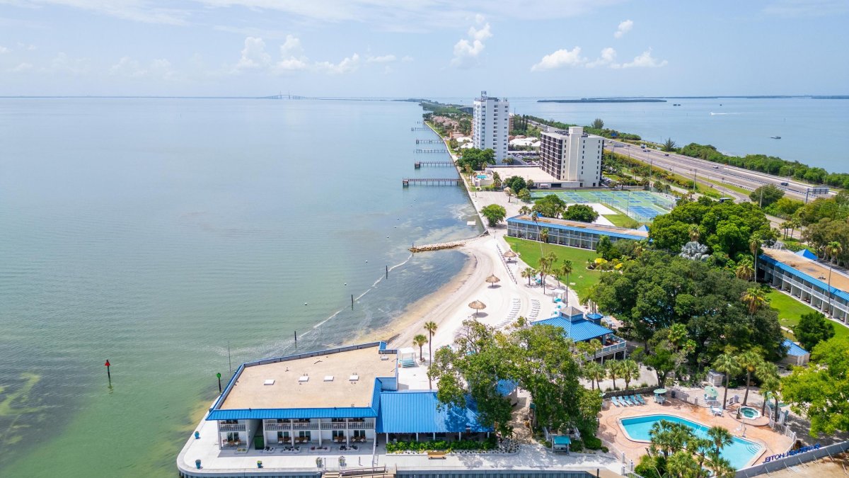 an aerial view of a waterfront hotel with a pool and pickleball courts