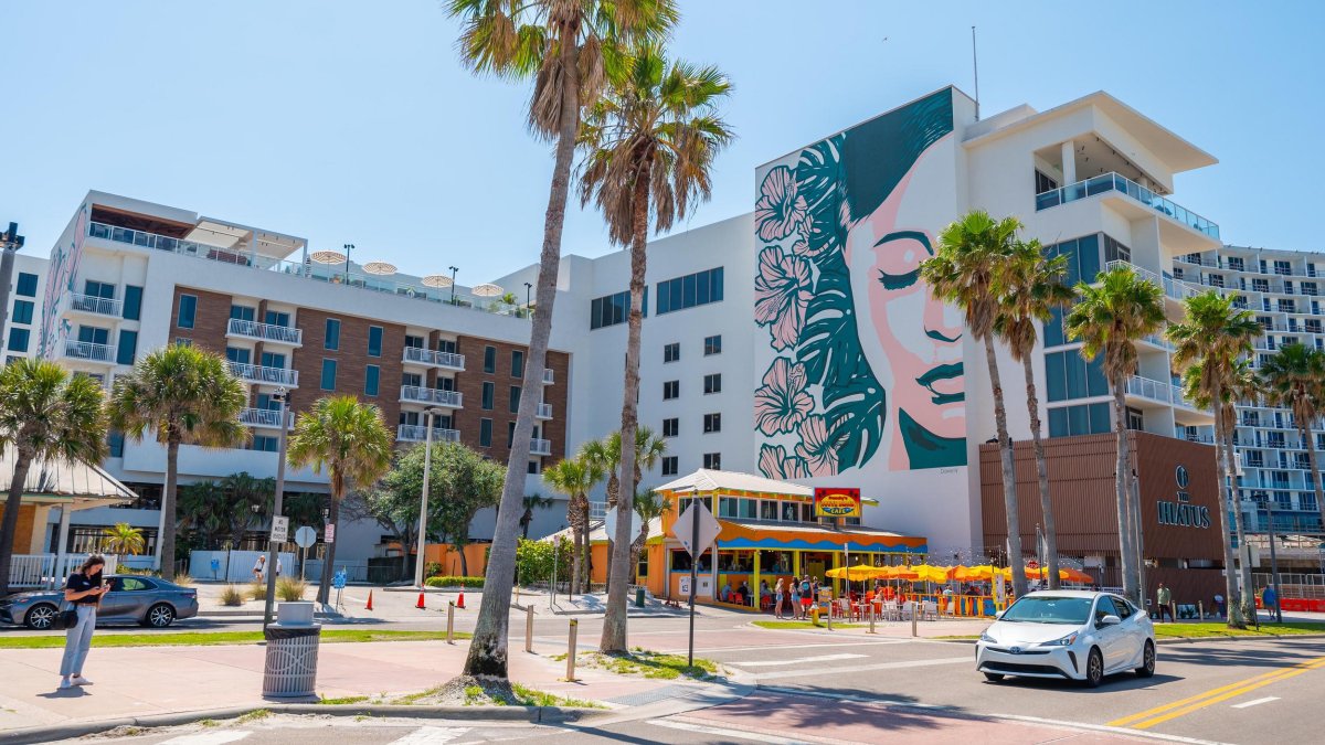exterior of a hotel with palm trees and a mural of a beautiful woman's face