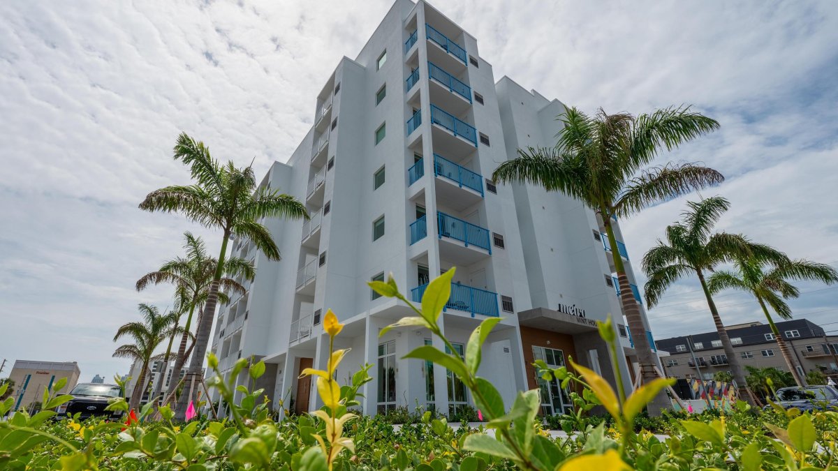 large modern white hotel with balconies with blue railings surrounded by palm trees