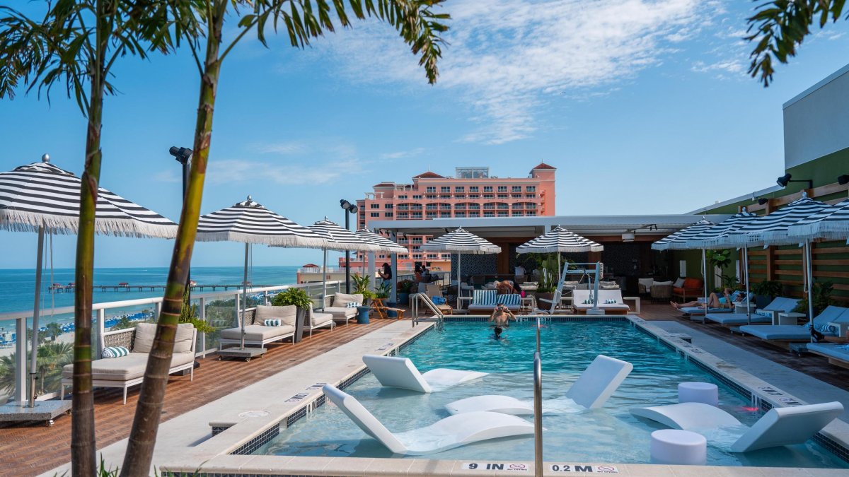 a hotel pool with lounge chairs in the water surrounded by palm trees with a view of the bay