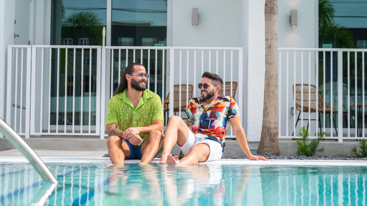 two smiling men in colorful shirts sit with their feet in the pool at Mint House