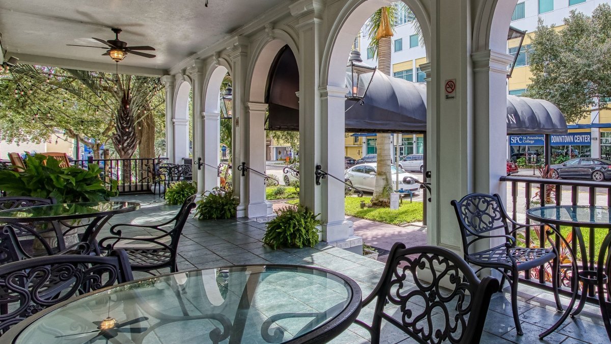 wrought iron chairs and tables with glass tops in a large outdoor patio at a hotel with curved archways