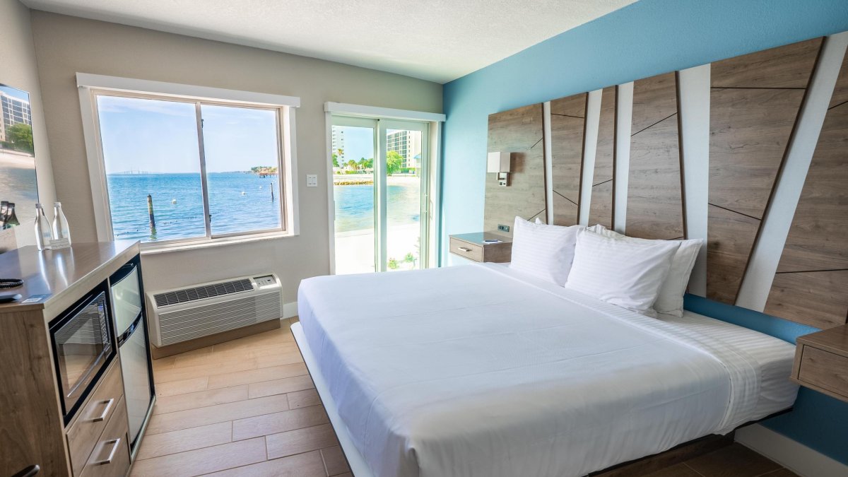 a hotel room with a bed with white linens and a modern geometric headboard with a great view of the blue bayfront waters