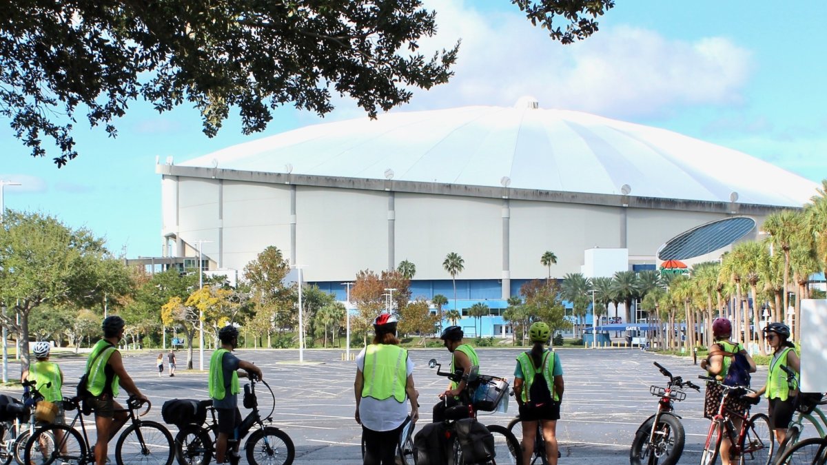 a group of bike riders in yellow safety vests stops to listen to a tour guide