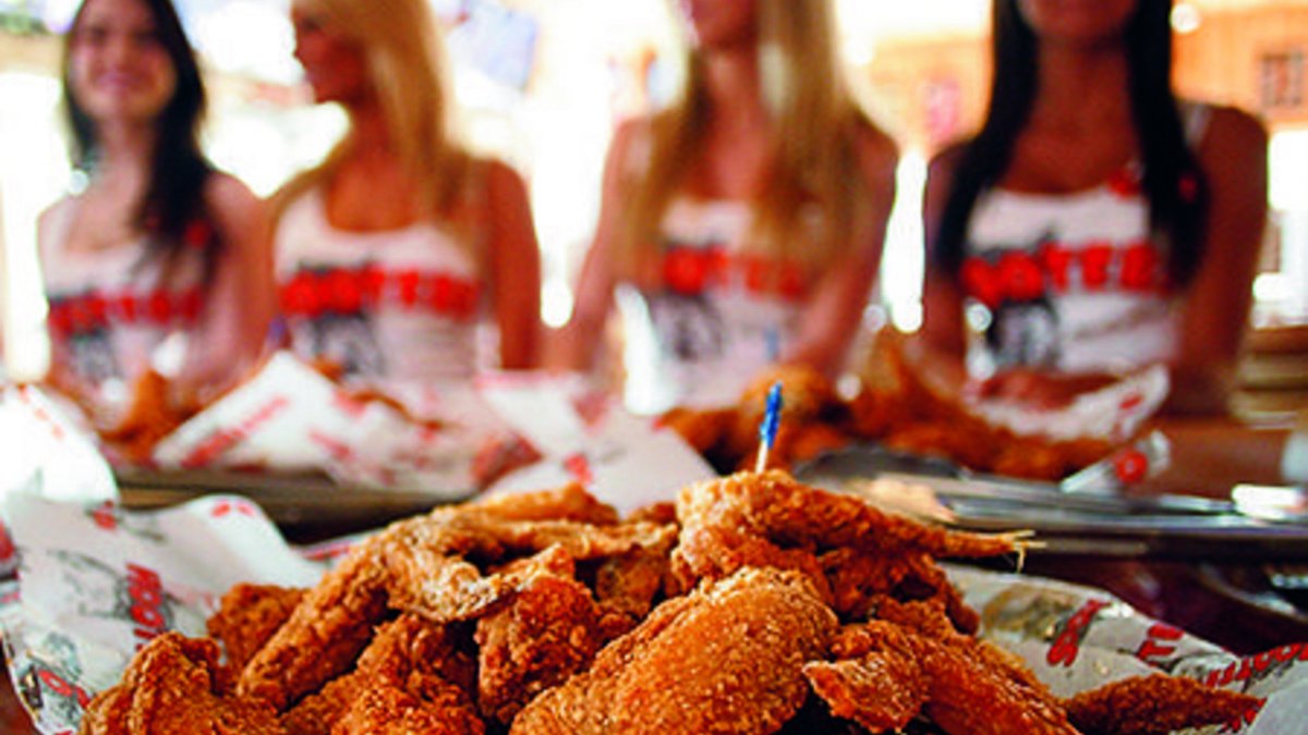 A plate of chicken wings and Hooters waitresses in the background