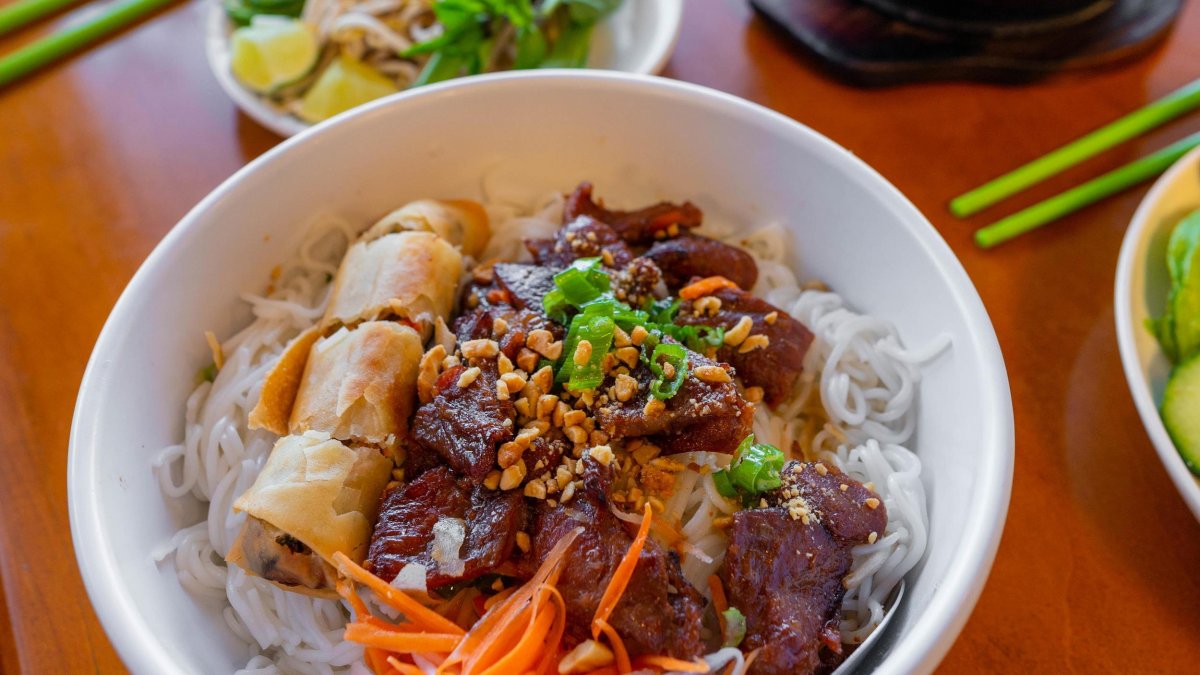 a bowl with white rice, a spring roll, an asian beef entree and decorated with pickled vegetables
