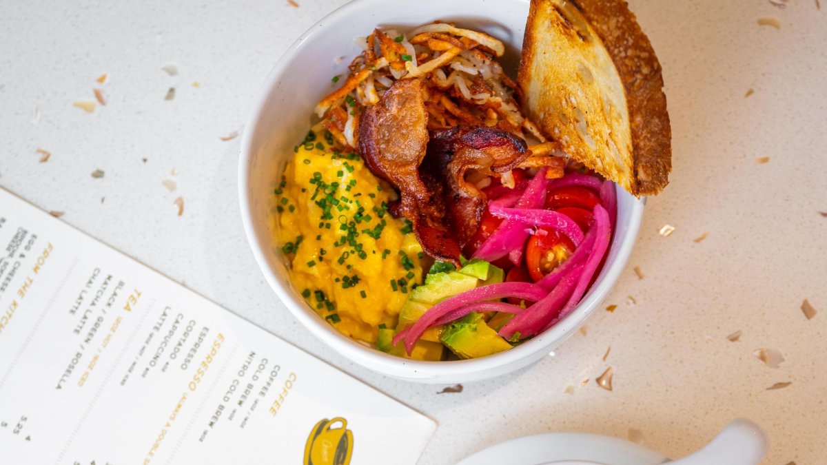 an artfully prepared breakfast bowl next to a menu and a pretty cup of latte