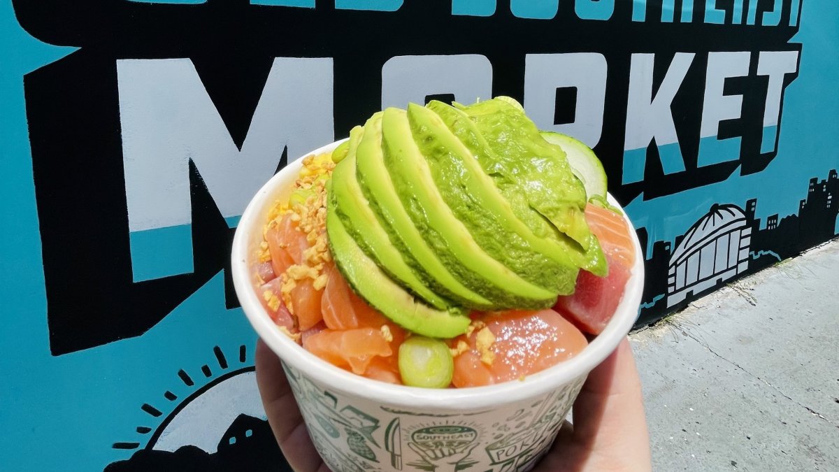 a hand holding a paper bowl with poke topeed with guacamole swirl