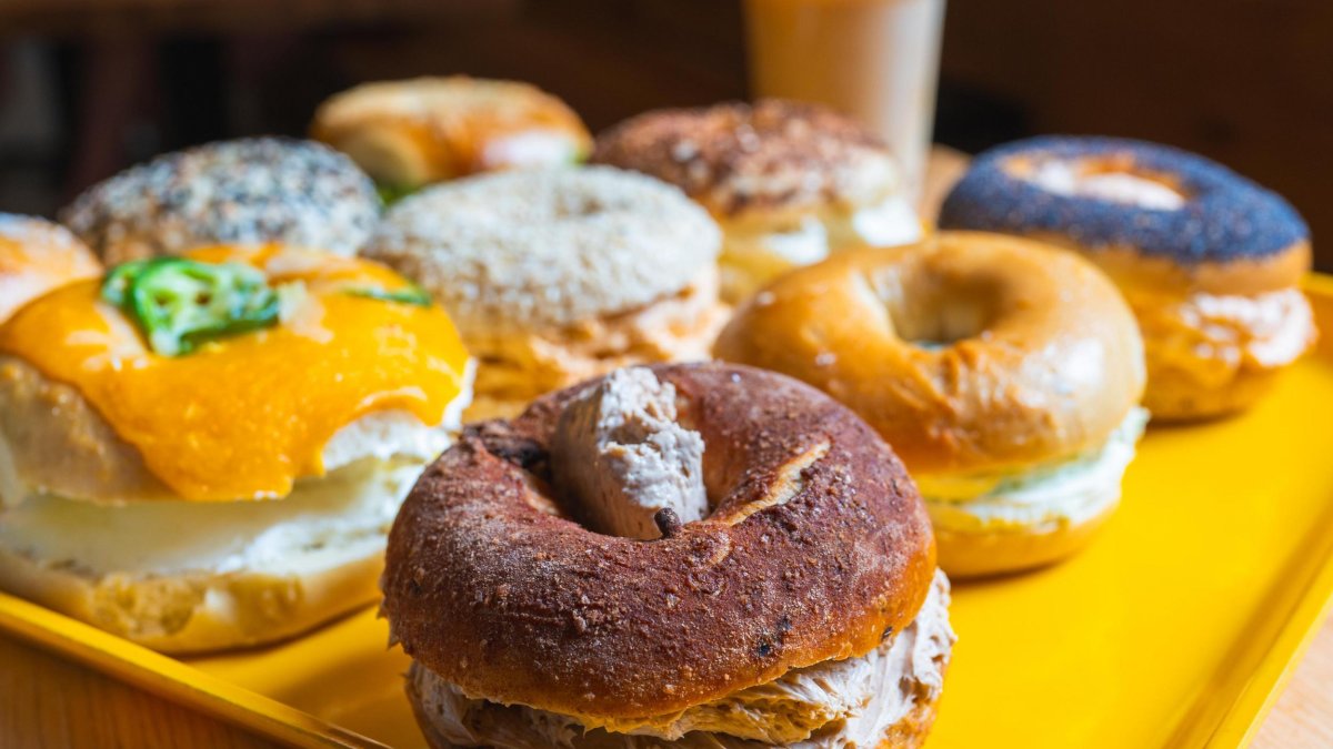 a yellow tray holding bagel sandwiches of many kinds, with an iced coffee in the background