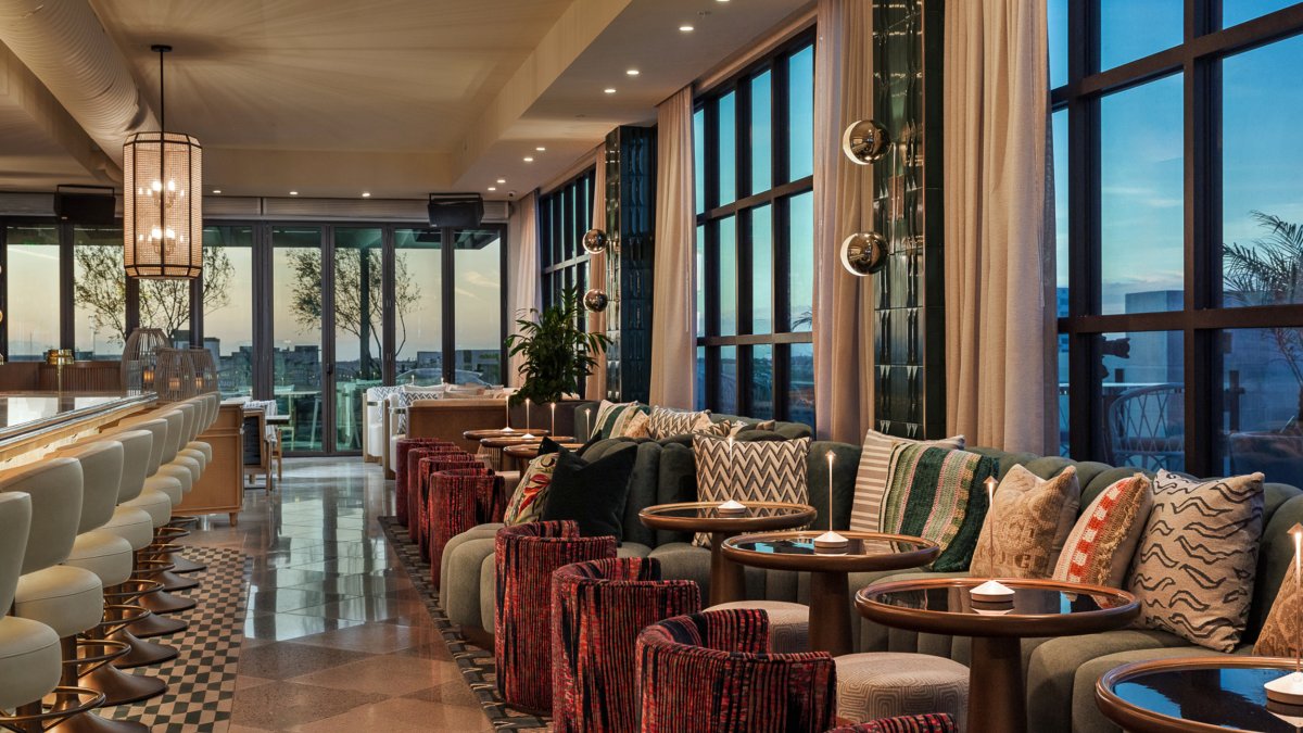 a stylish bar with small tables to the side and views of a city through large windows