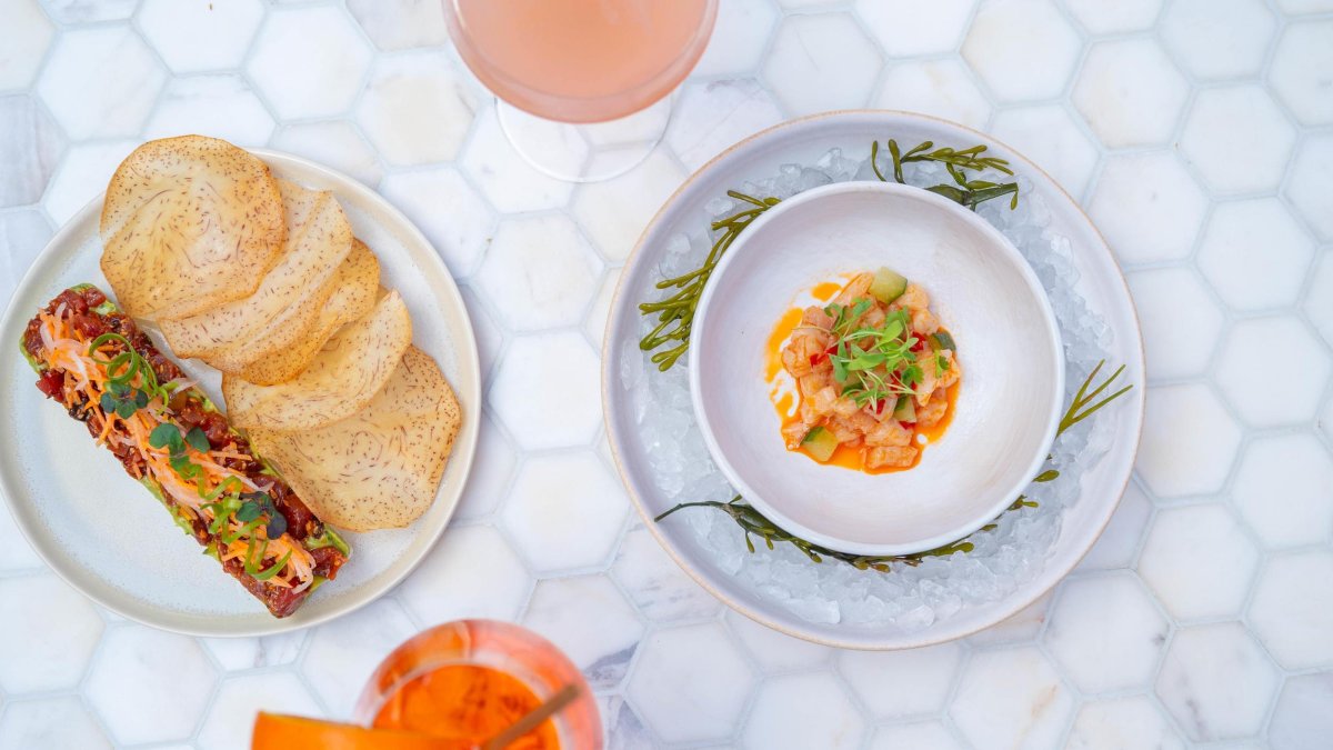 two cocktails and two appetizers set on a table with small white hexagonal tiles