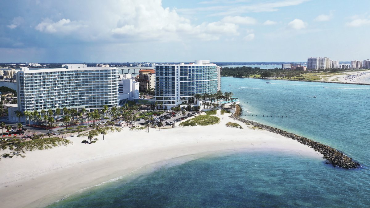 two beachfront hotels with multiple floors set on a white sand beach and blue waters