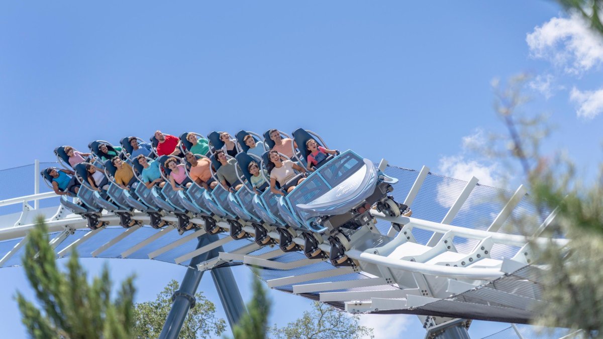 seaworld orlando's new roller coaster penguin trek on a white roller coaster track as guests ride high in teh sky over trees below.
