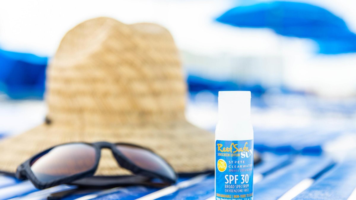 uma toalha de praia com um chapéu de palha, óculos escuros e um pequeno frasco de protetor solar seguro para recifes