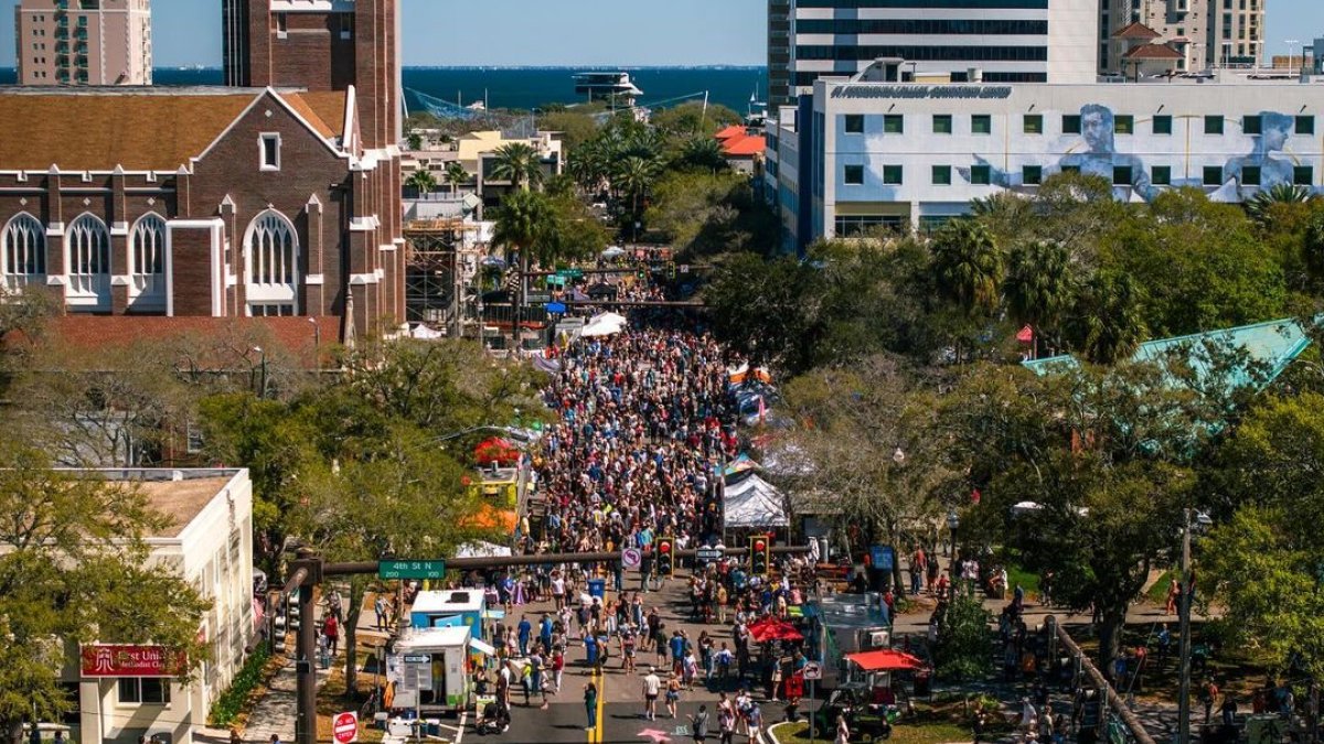 Aerial drone view of an outside street market during the day by the St. Pete waterfront featuring lots of people.