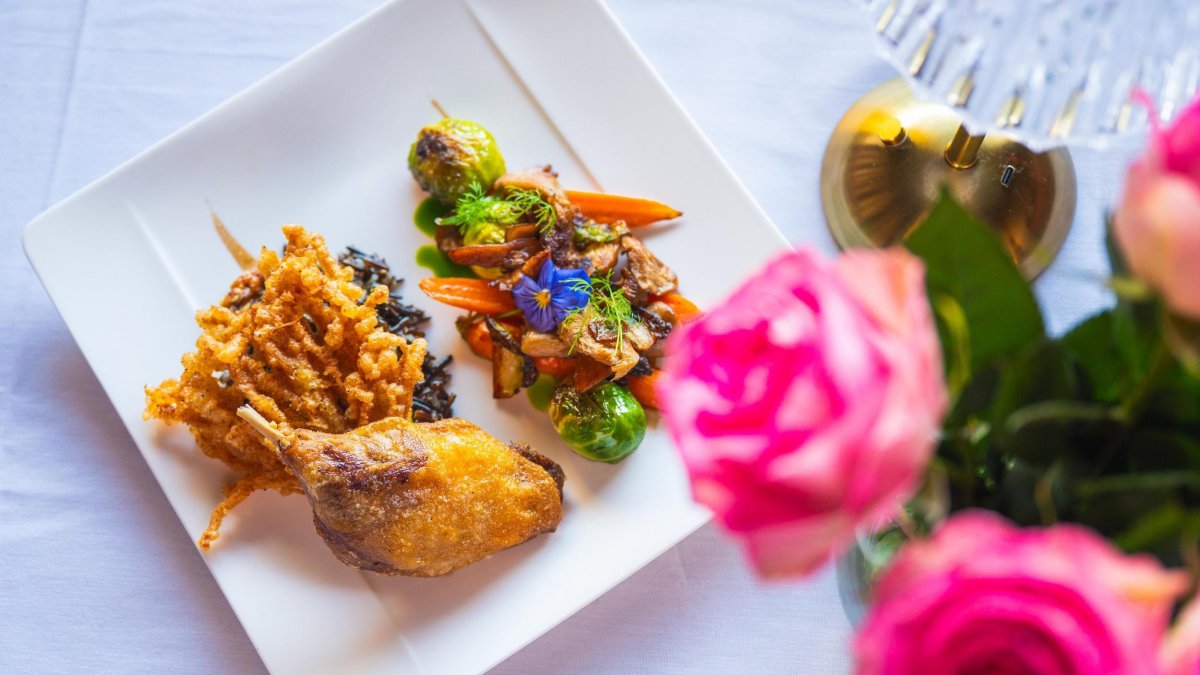 A view of a beautifully plated dish at Black Pearl Restaurant in Dunedin, accompanied by bright pink roses on the white linen tablecloth