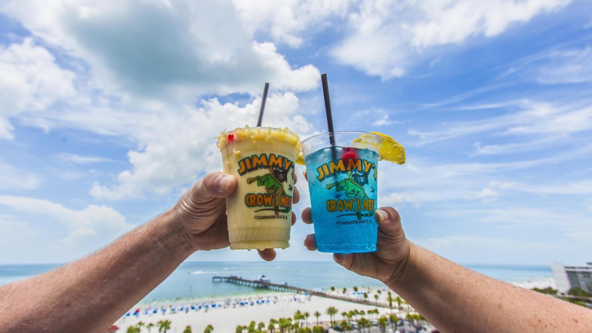 two tropical drink in a Jimmys Crow's Nest plastic cup cheersing with rooftop view in background of Clearwater Beach and Pier