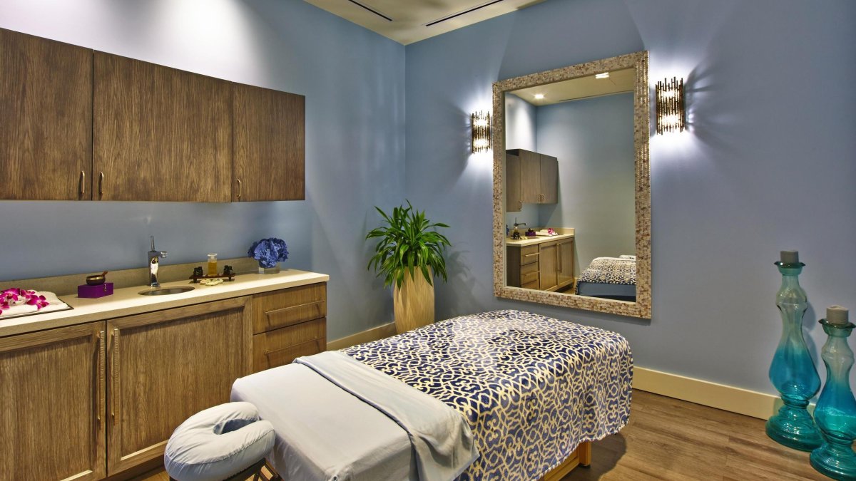 an elegant spa treatment room in soothing wood tones with a massage table that has a black and white blanket on top of it