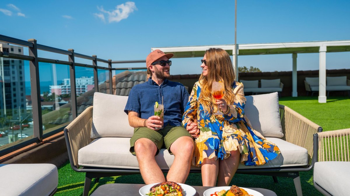 man and woman sitting on outdoor couch looking at each other enjoying drinks on rooftop