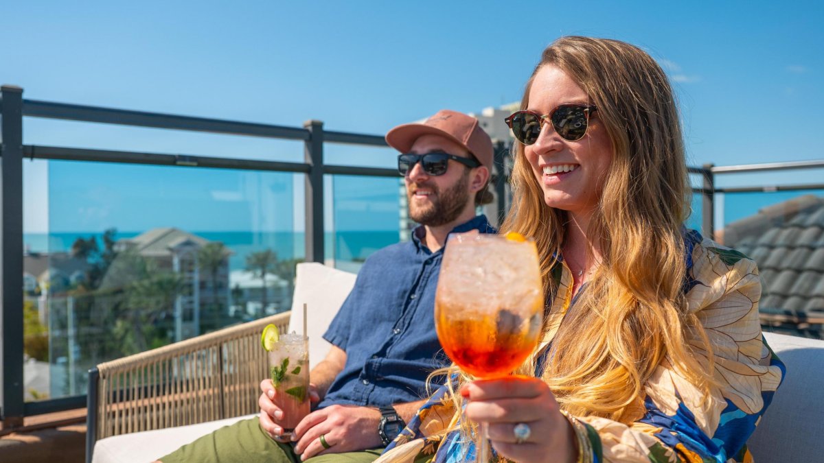 woman and man holding cocktails sitting outside on rooftop smiling